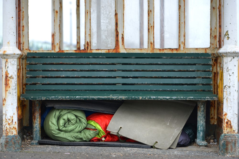Photo of a bench with a homeless person's supplies underneath