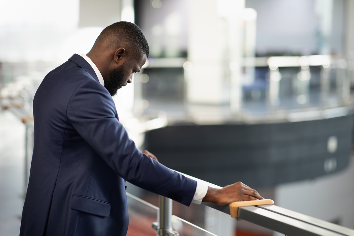 Stressed african american young man in suit entrepreneur standing by railing with head down, experiencing difficulties at work, back view shot, panorama with copy space, financial crisis and business