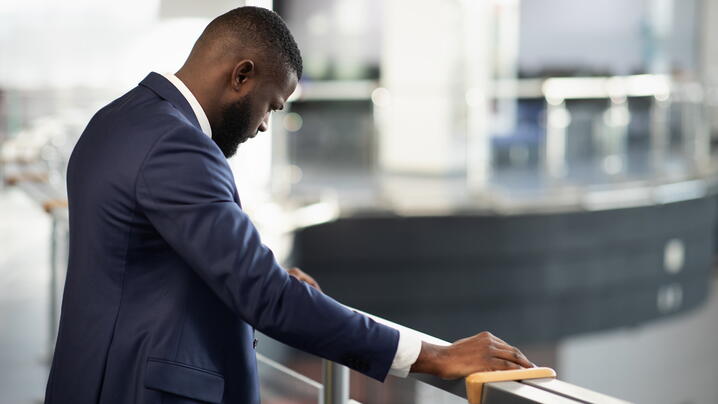Stressed african american young man in suit entrepreneur standing by railing with head down, experiencing difficulties at work, back view shot, panorama with copy space, financial crisis and business