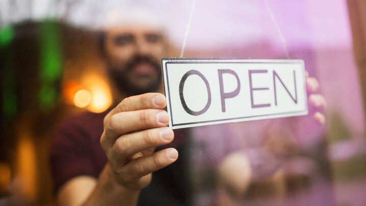 Image of person turning around an "Open" sign on a business