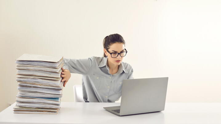 Image showing woman pushing a stack of papers aside in favor of a laptop