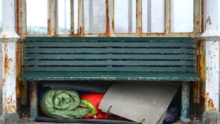 Photo of a bench with a homeless person's supplies underneath