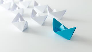 Blue origami paper boat leading multiple white boats